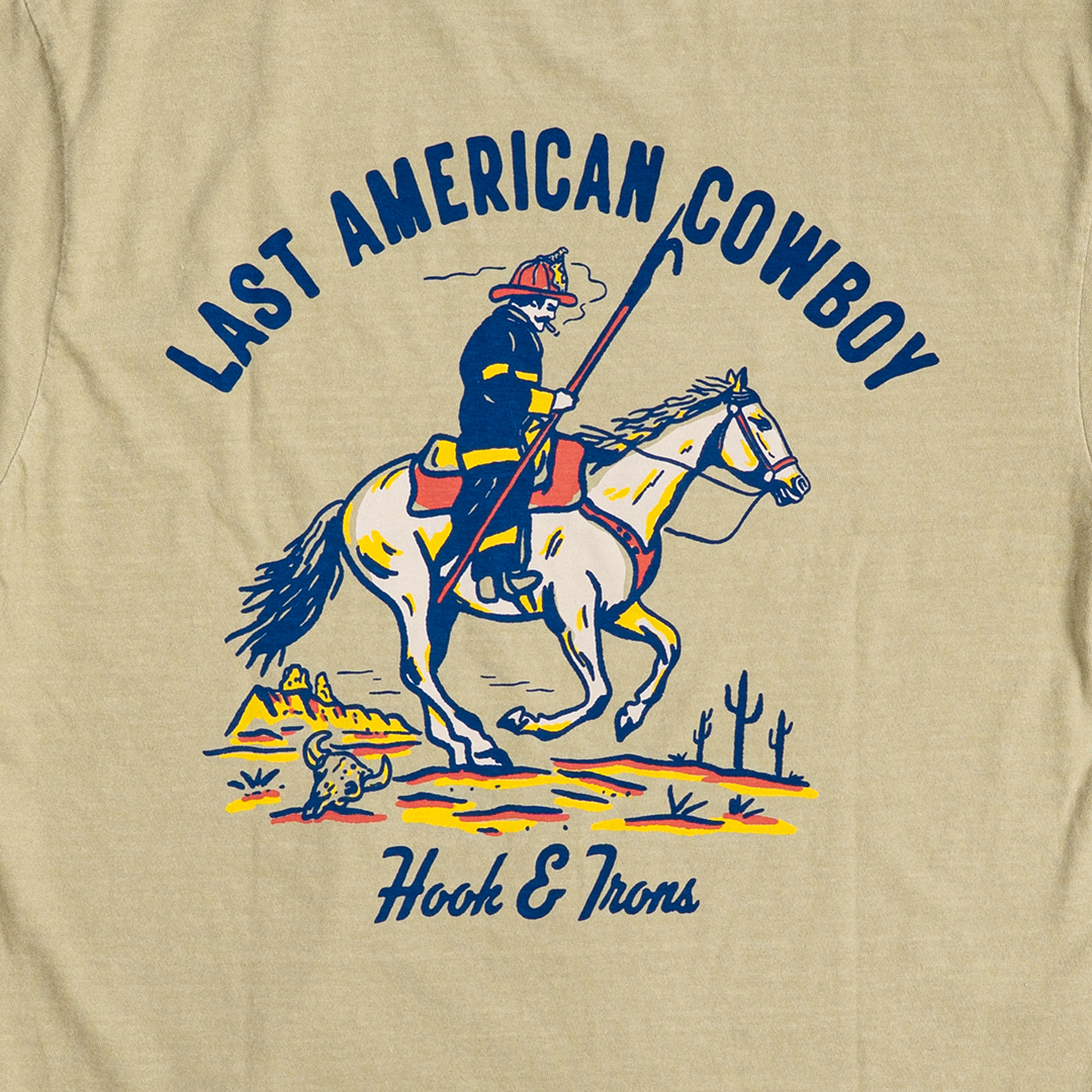 Khaki t-shirt with a graphic of a cowboy on a horse and text 'Last American Cowboy' and 'Hook & Irons'.