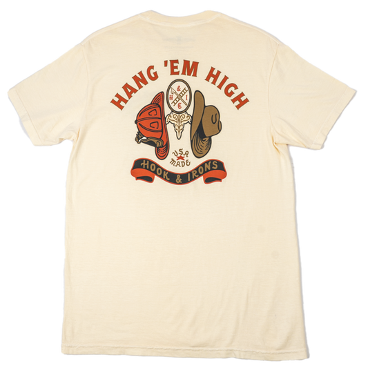 A cream-colored short-sleeve t-shirt shown from the back, featuring a large graphic print with the words 'HANG 'EM HIGH' in red arched lettering above a dreamcatcher, boots, and a banner reading 'Hook & Irons'.