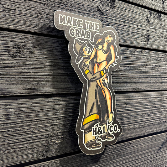 Metal sign with a design of a person holding a crab and text 'MAKE THE CRAB H&I CO.' on a wooden surface.